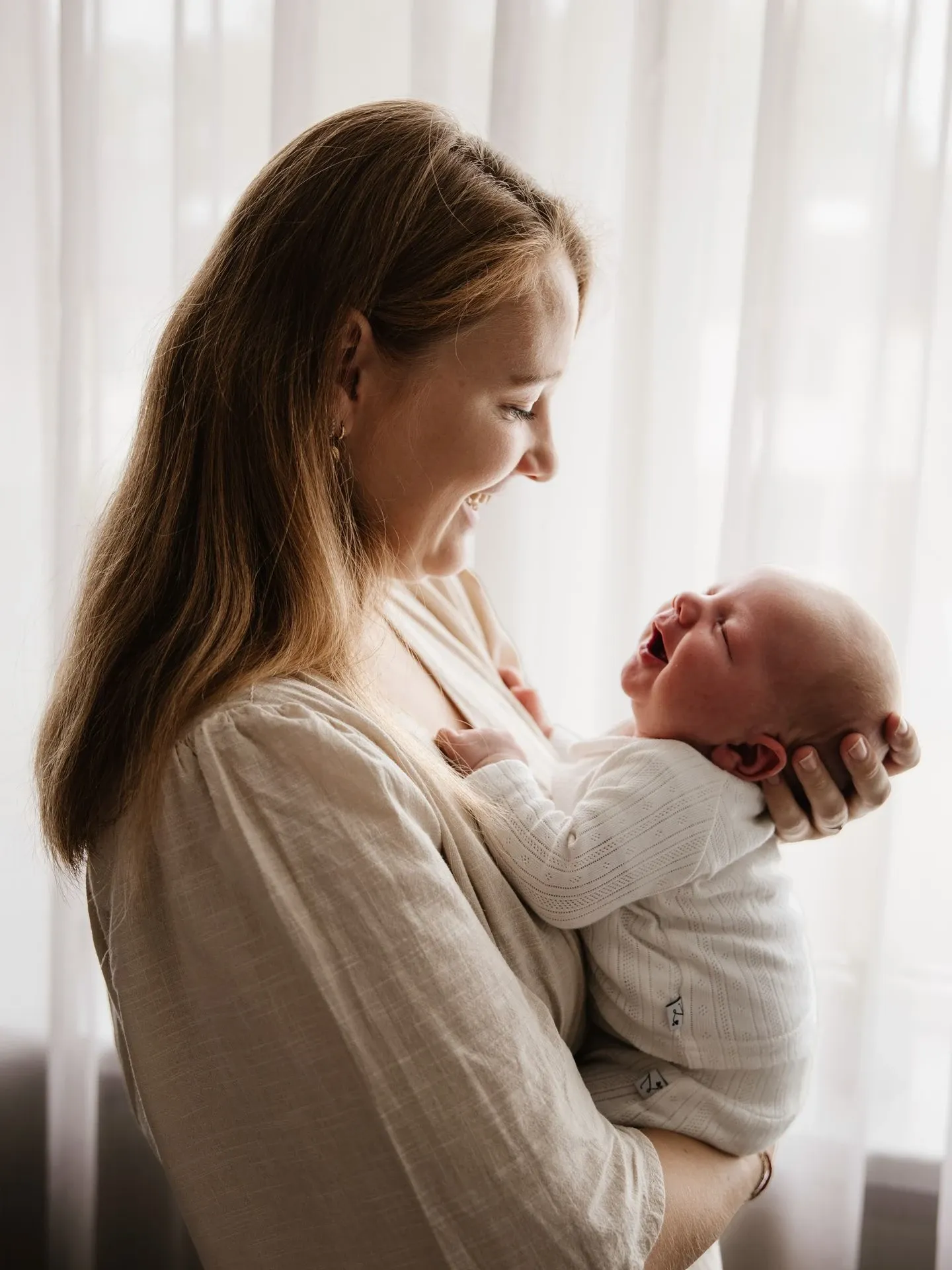 Lachende mama bij het raam tijdens de newbornshoot